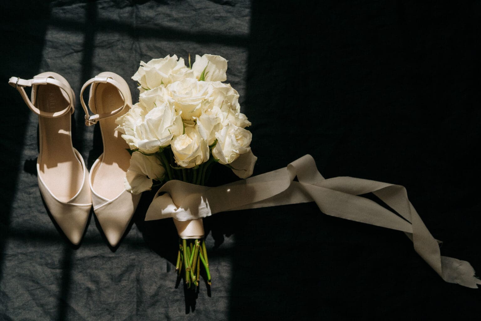bridal shoes and bouquet laying on black backdrop