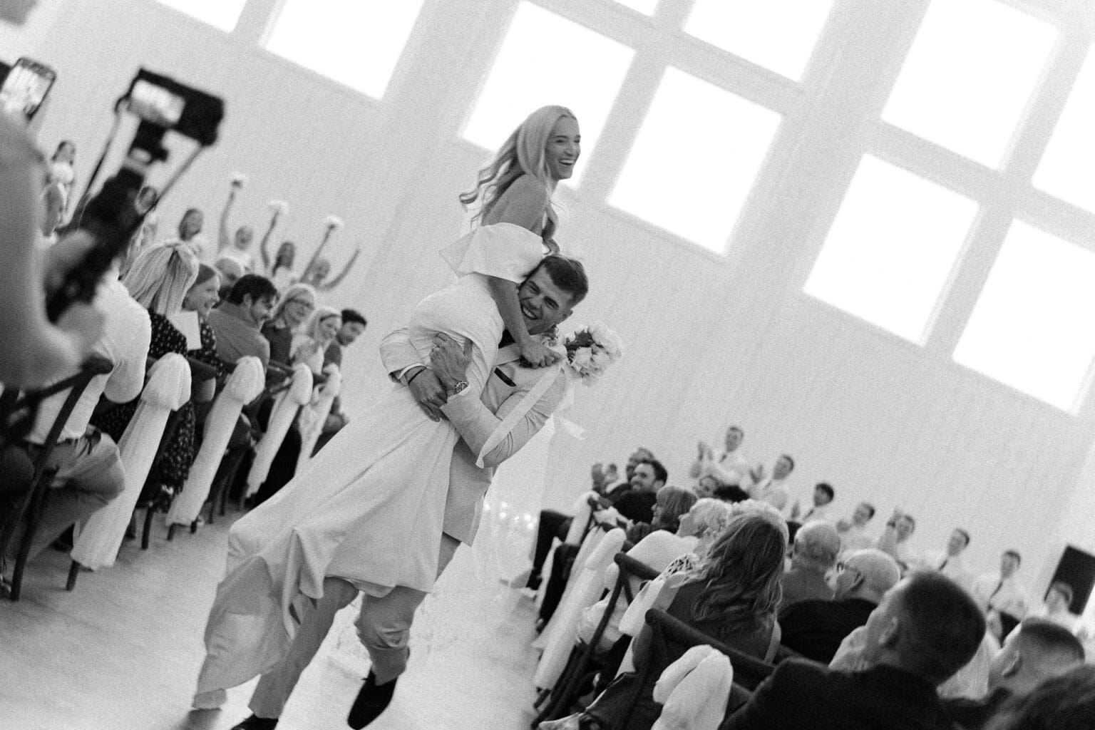 black and white timeless photo of groom carrying bride down the aisle