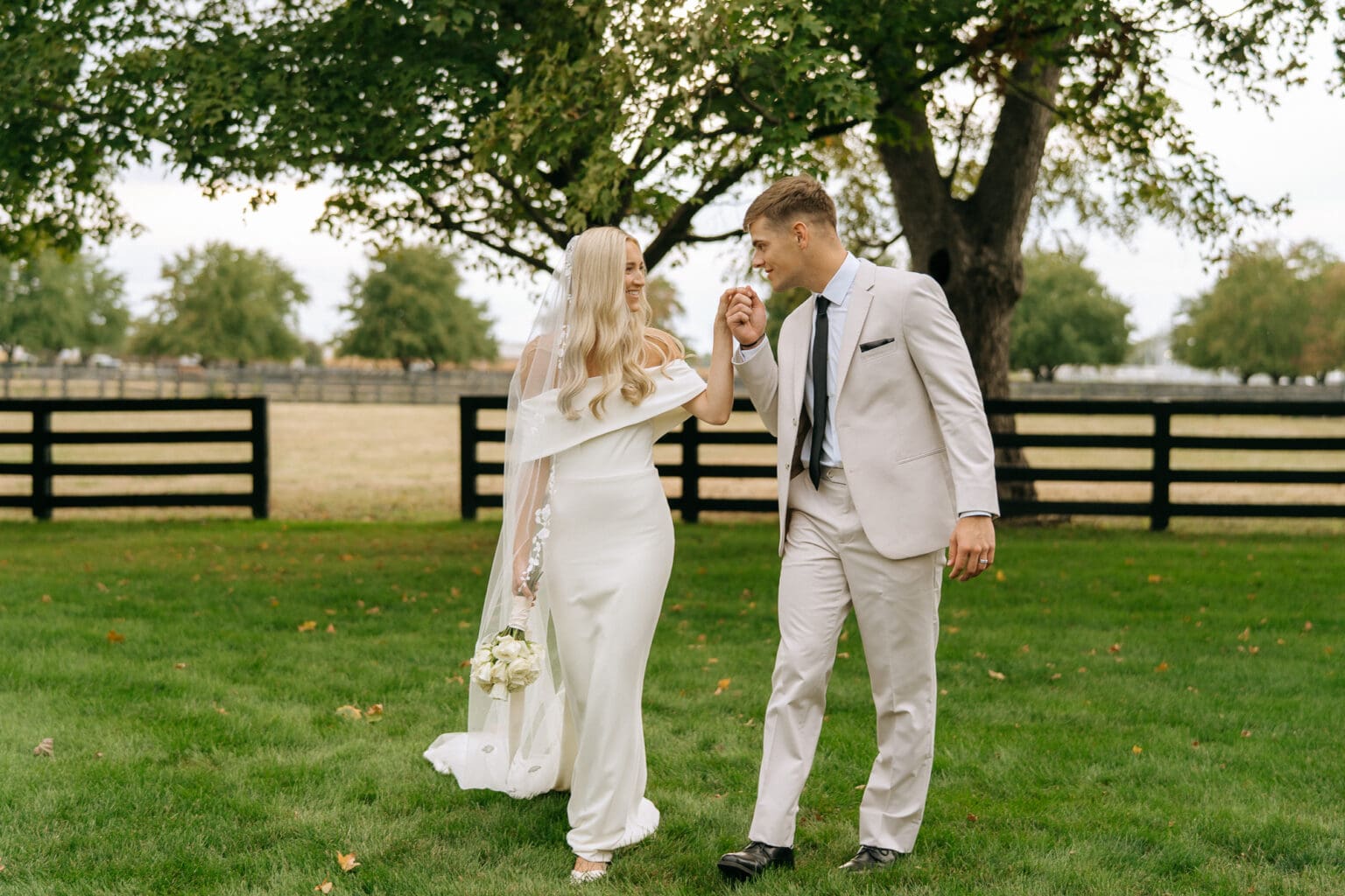 bride and groom walking in grass and carrying ivory floral bouquet