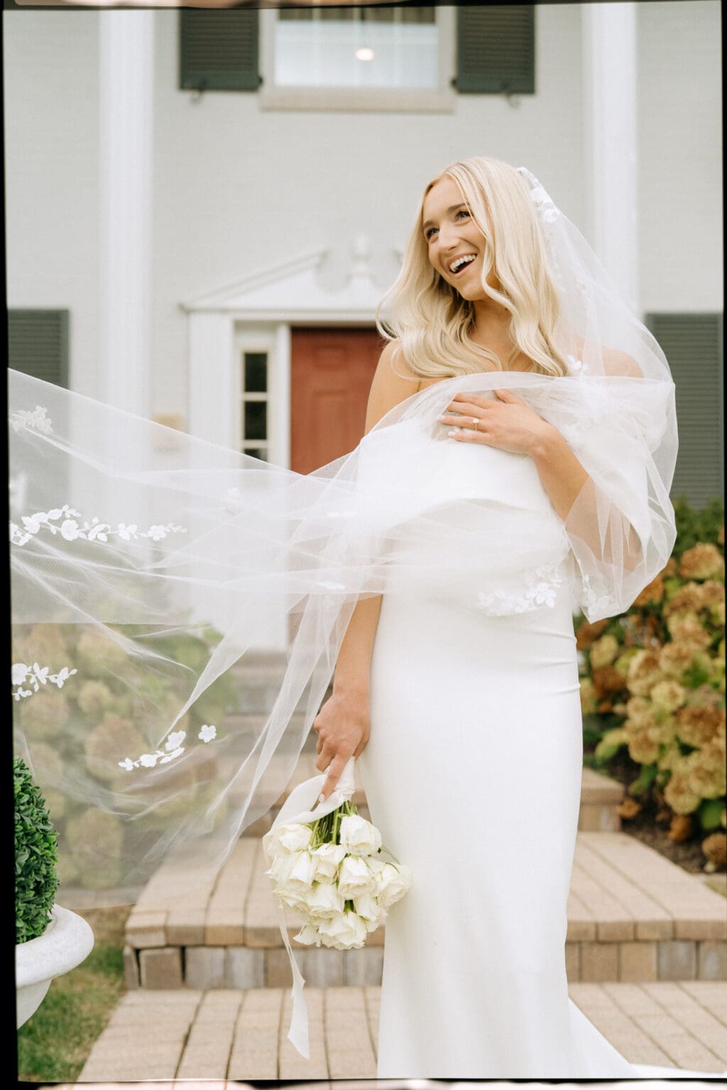 Bride laughing and wearing long veil with ivory bouquet